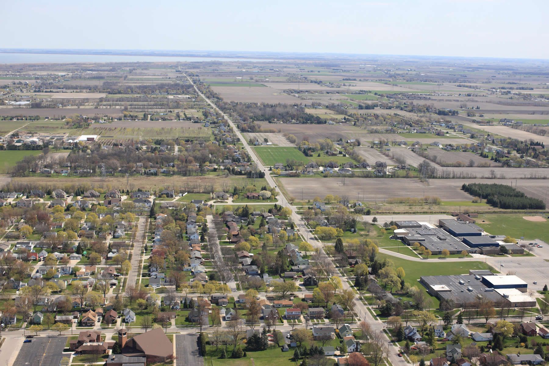 Aerial view over an east Michigan town where streets give way to section-line farmland, with Saginaw Bay on the horizon.